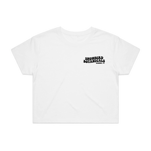 White Crop Top with a Groovy font print on the left chest saying "Snowbird Botanicals Barnet, VT".
